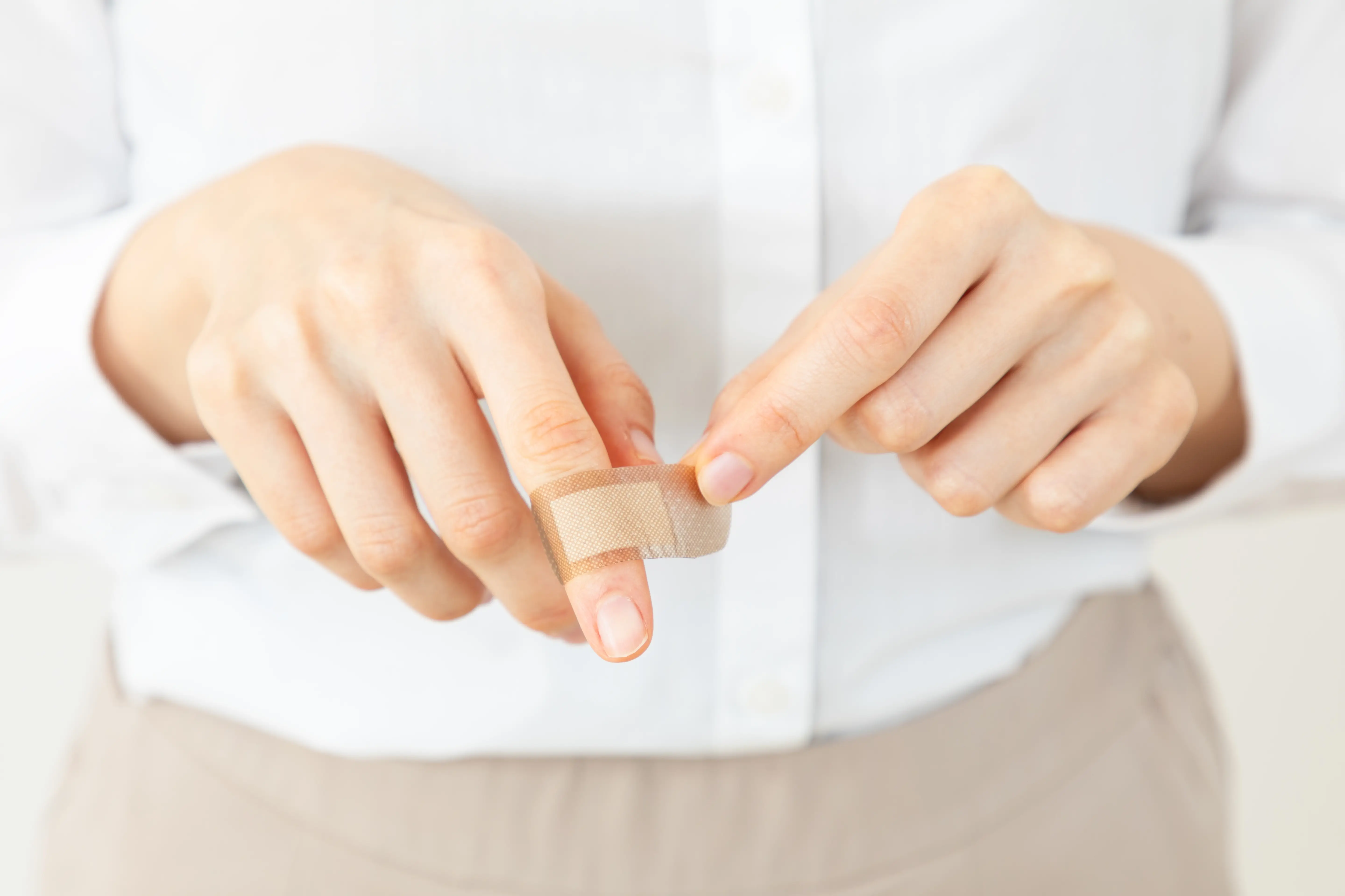 Frau bringt Pflaster auf ihrer Schnittwunde am Finger an.